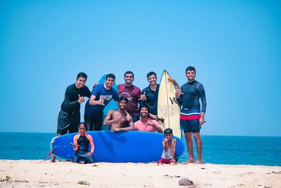 A group of nine on the sand at Panambur behind two surfboards, several of them throwing a shaka, two children in front
