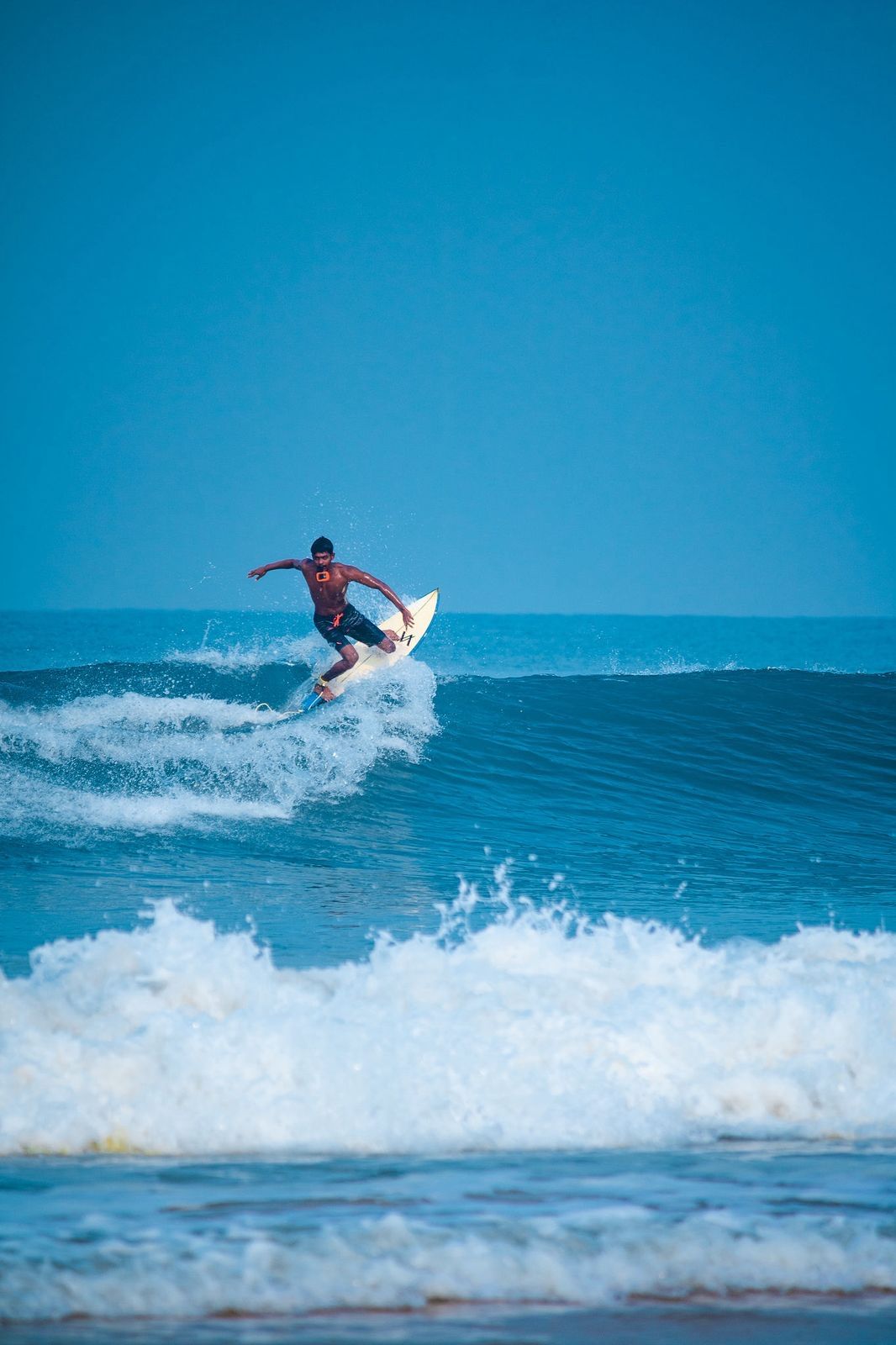A surfer turning off the top of a small blue wave, spray coming off the tail