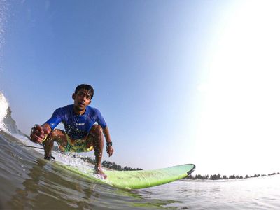 Movin crouched low on a green board, filmed from the water a few feet in front of him