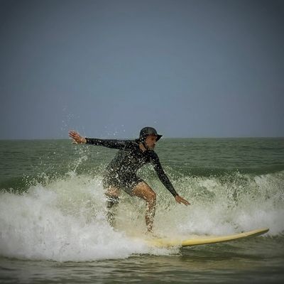 Rohan in a black rash guard and bucket hat, low over a yellow board as it turns through the white water