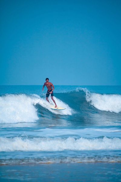A surfer riding a small broken wave on a shortboard under a clear blue sky